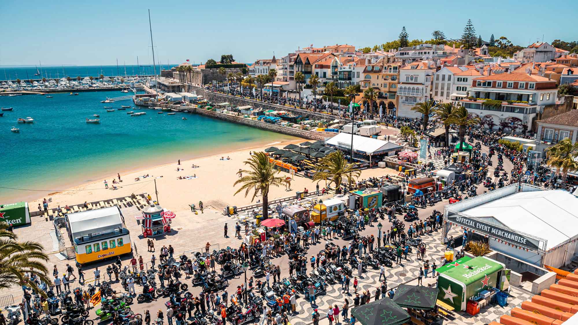 Bikers on a beach by a harbour.