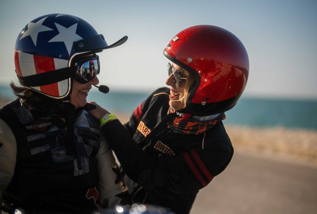 Two HOG Members with colourful motorcycle clothes and crash helmets smiling at each other